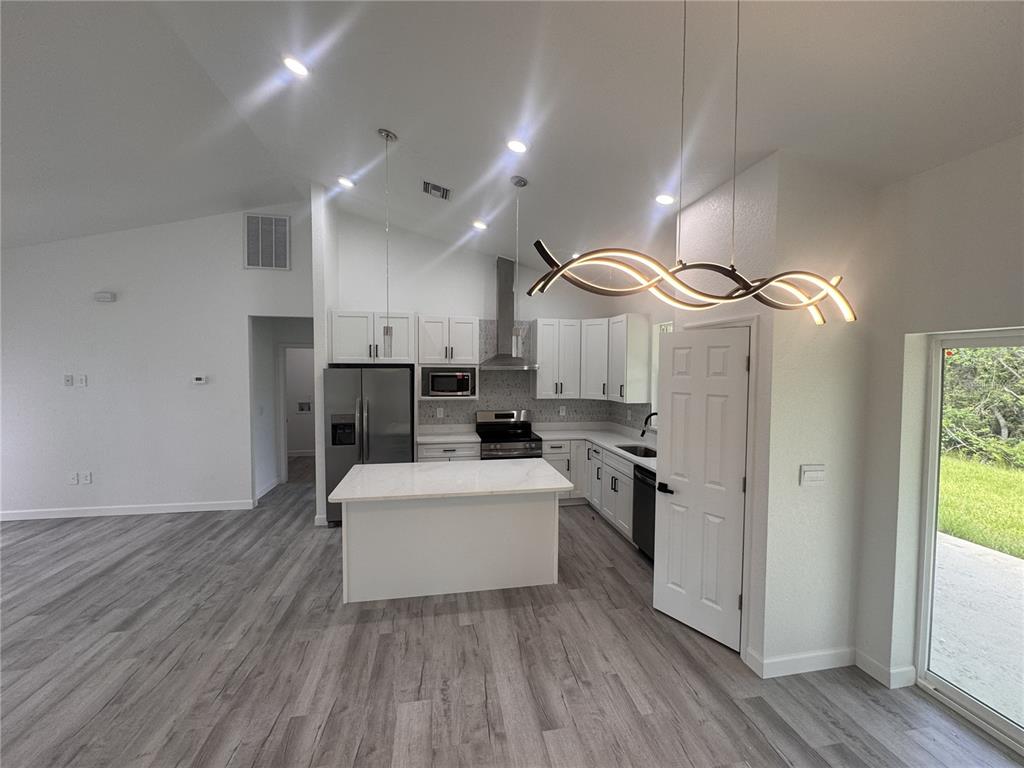 A modern kitchen features white cabinetry, a central island, and a distinctive wavy pendant light — 7624 ANCHA STREET, SEBRING, FL