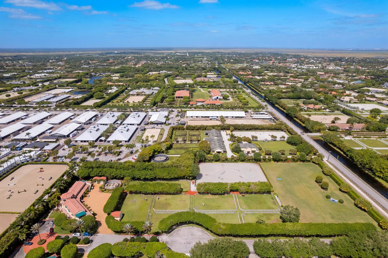 An aerial view shows an equestrian facility with stables, riding arenas, and fenced paddocks — 3151 Hickstead Place, Wellington FL 33414, WELLINGTON, FL