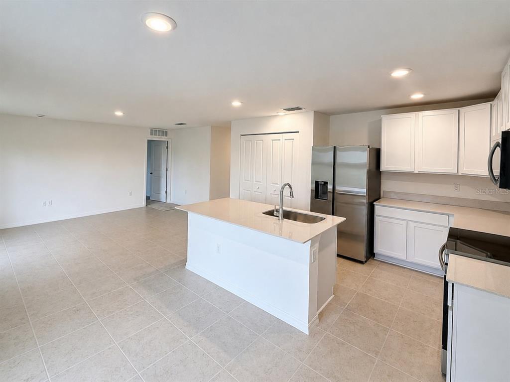 A kitchen with white cabinets, a central island, and stainless steel appliances opens to a room — 1691 2ND AVENUE, DELAND, FL