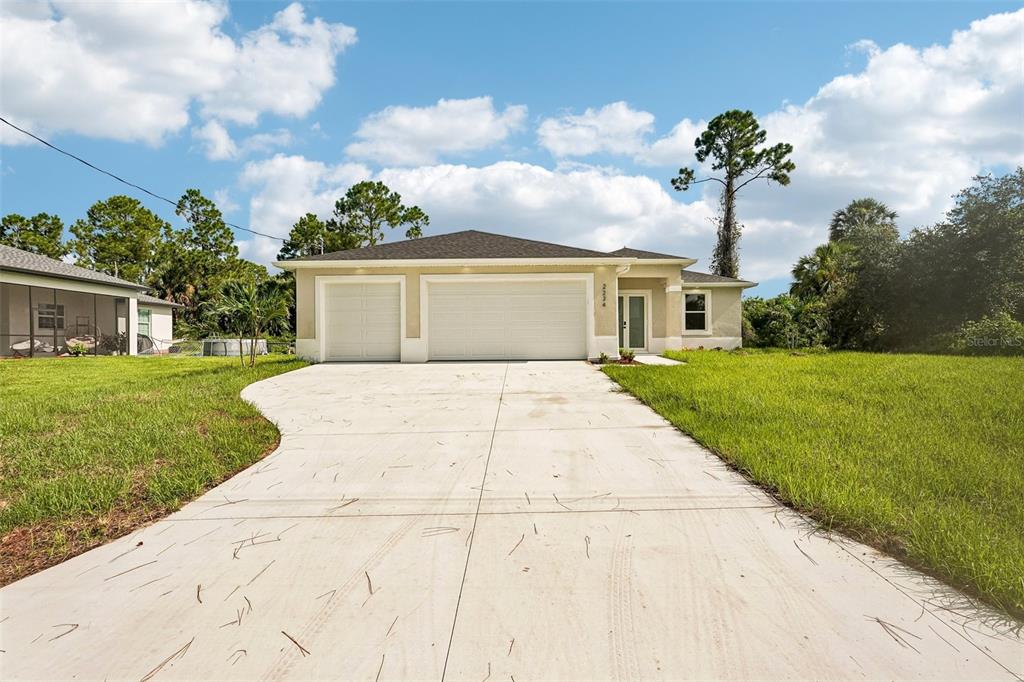 A single-story house with a three-car garage and a concrete driveway under a cloudy sky — 2234 JAMESON AVENUE, NORTH PORT, FL