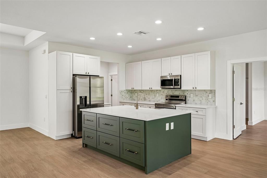 A kitchen features white upper cabinets, a green island with a white countertop, and wood flooring — 2234 JAMESON AVENUE, NORTH PORT, FL