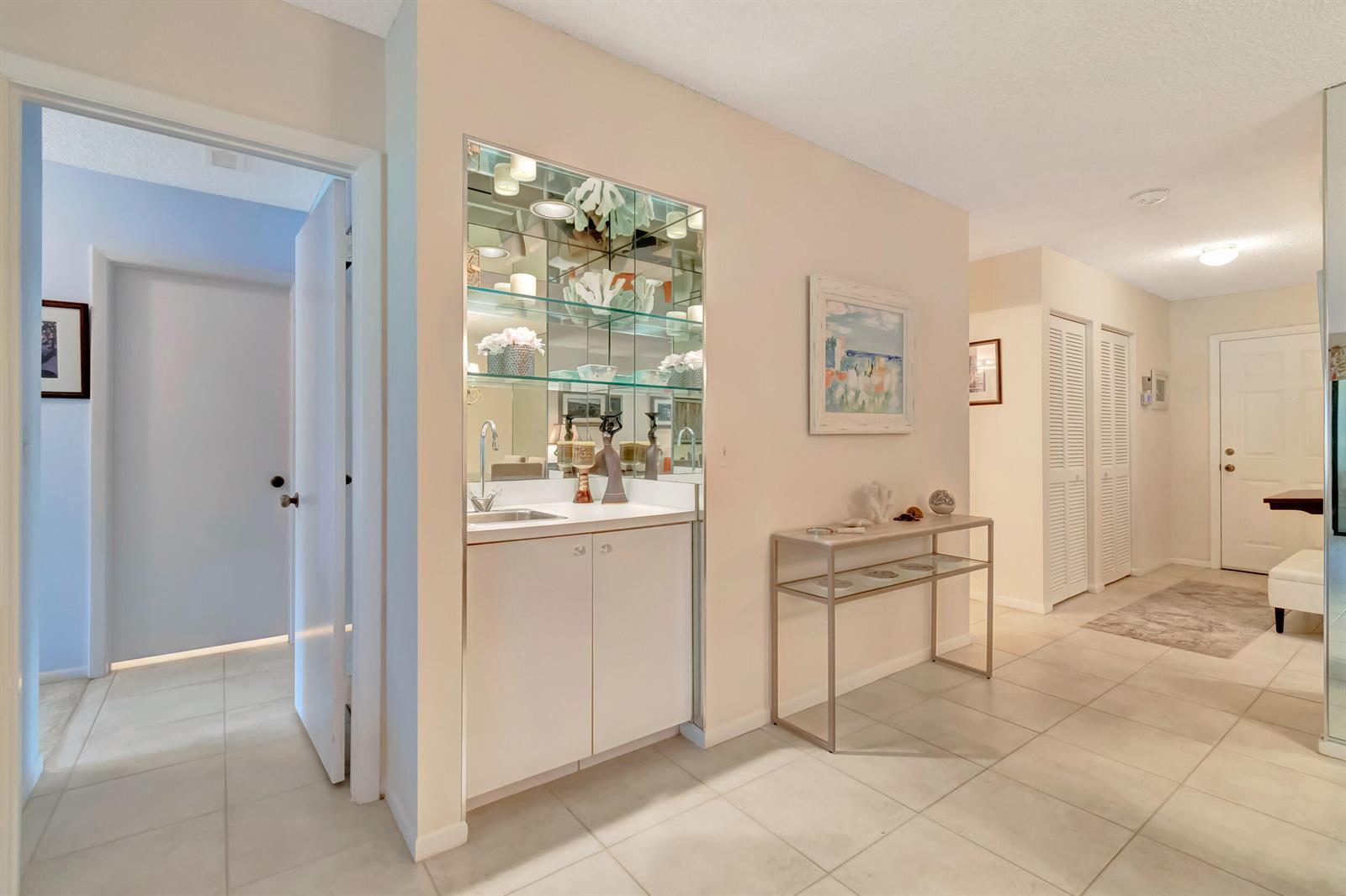 A hallway features a wet bar with mirrored shelving, a console table, and tiled flooring — 19 Westgate Lane # 19f, Boynton Beach FL 33436, BOYNTON BEACH, FL