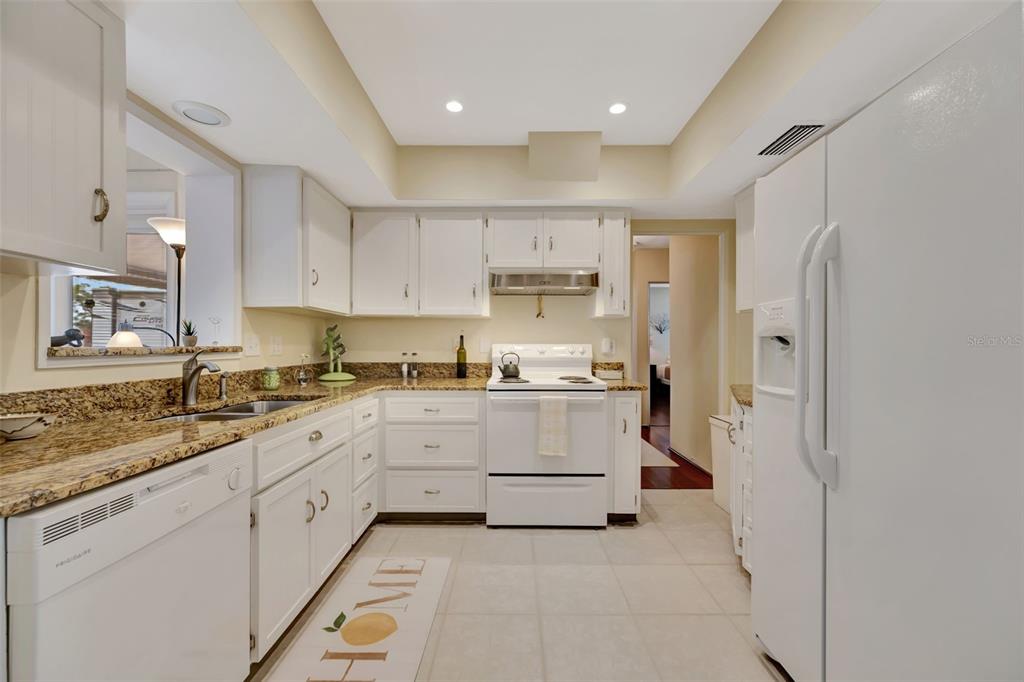 A kitchen features white cabinets, granite countertops, white appliances, and light-colored tile flooring — 130 59TH STREET W, BRADENTON, FL