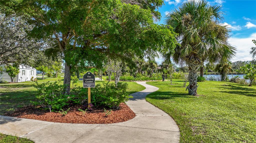 A paved walkway winds through a grassy park area with trees and a garden sign — 9357 AGATE STREET, PORT CHARLOTTE, FL