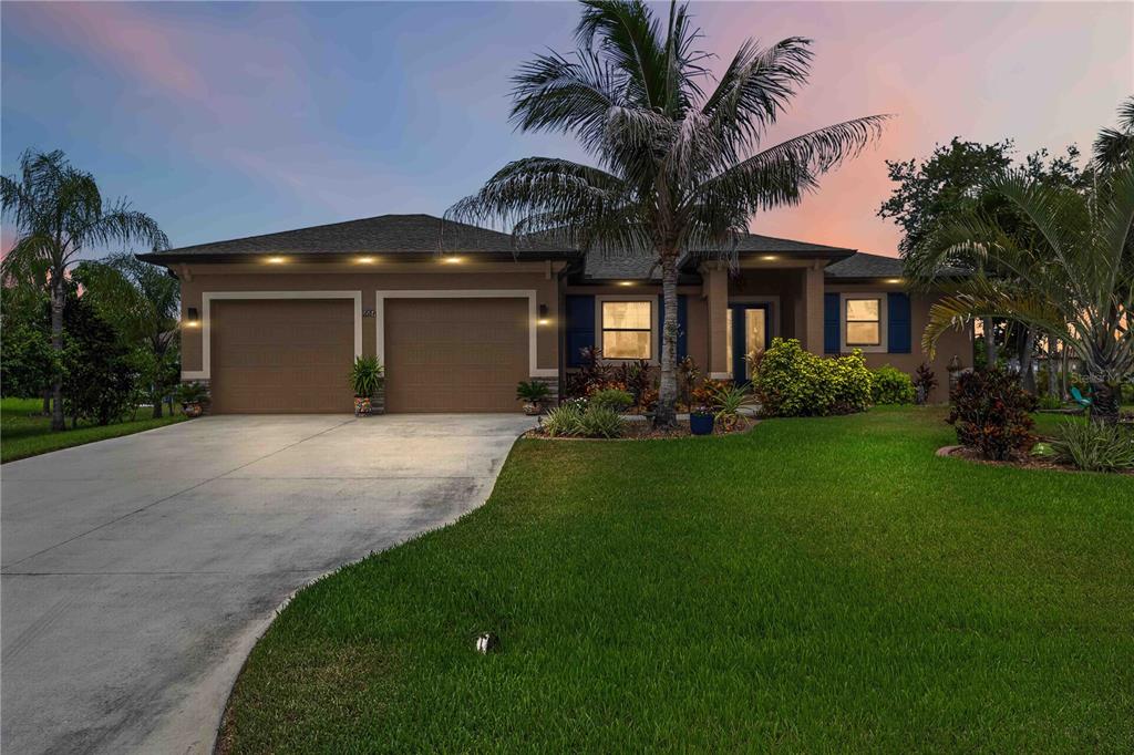 A single-story house with a two-car garage, palm trees, and a concrete driveway at dusk — 227 LONG MEADOW LANE, ROTONDA WEST, FL