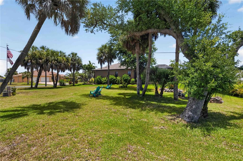A grassy yard features several palm trees, two teal chairs, and a house in back — 227 LONG MEADOW LANE, ROTONDA WEST, FL