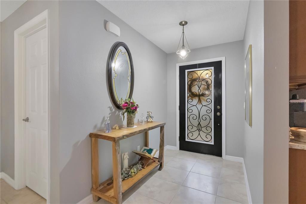 An entryway features a black front door with decorative glass, a wooden console table, and mirror — 21714 BELGIAN COURT, MOUNT DORA, FL
