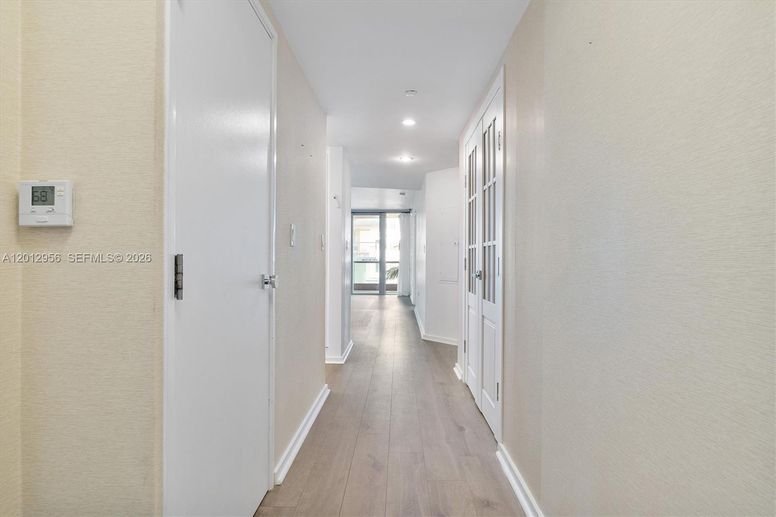 A hallway with light wood flooring leads toward a glass door opening to a balcony — 9401 Collins Ave # 505, Surfside FL 33154, SURFSIDE, FL