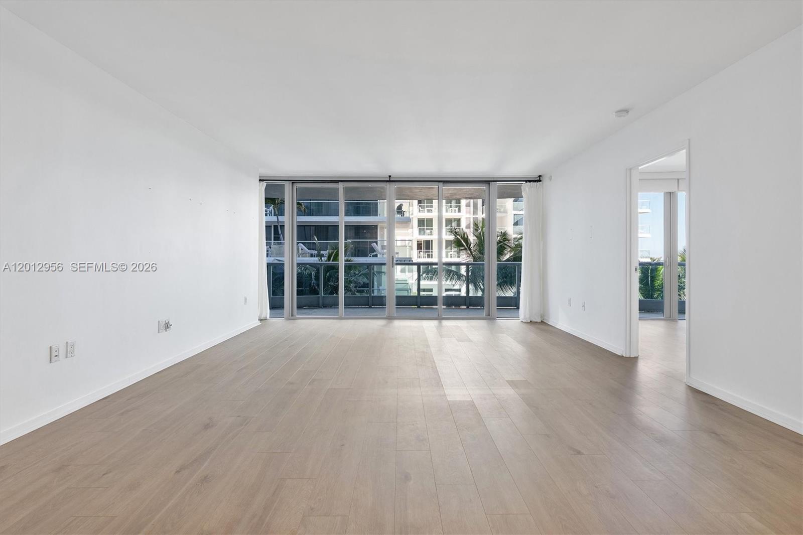 An empty living room with light wood flooring, white walls, and floor-to-ceiling glass sliding doors — 9401 Collins Ave # 505, Surfside FL 33154, SURFSIDE, FL