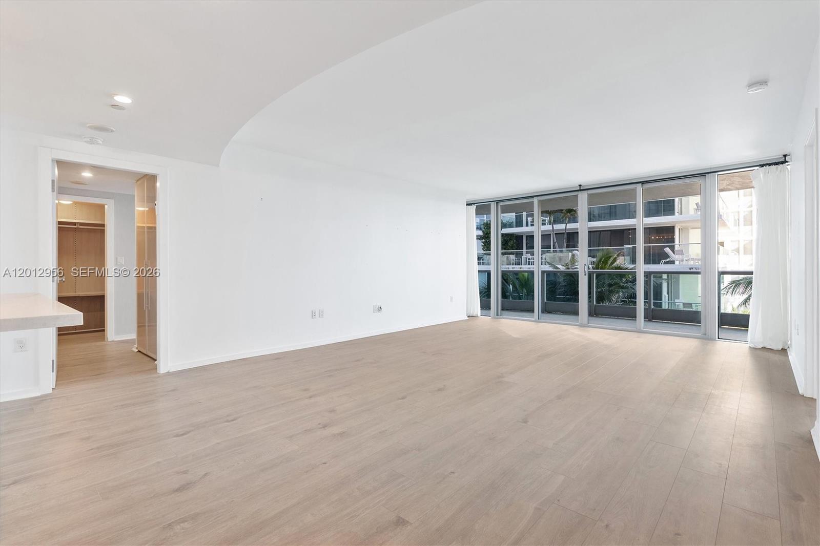 An empty room features light wood-look flooring, white walls, and a large sliding glass door — 9401 Collins Ave # 505, Surfside FL 33154, SURFSIDE, FL