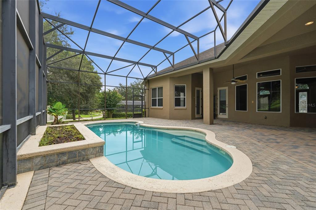 A screened-in patio features a swimming pool with a raised planter and paver decking — 17535 COBBLESTONE LANE, CLERMONT, FL