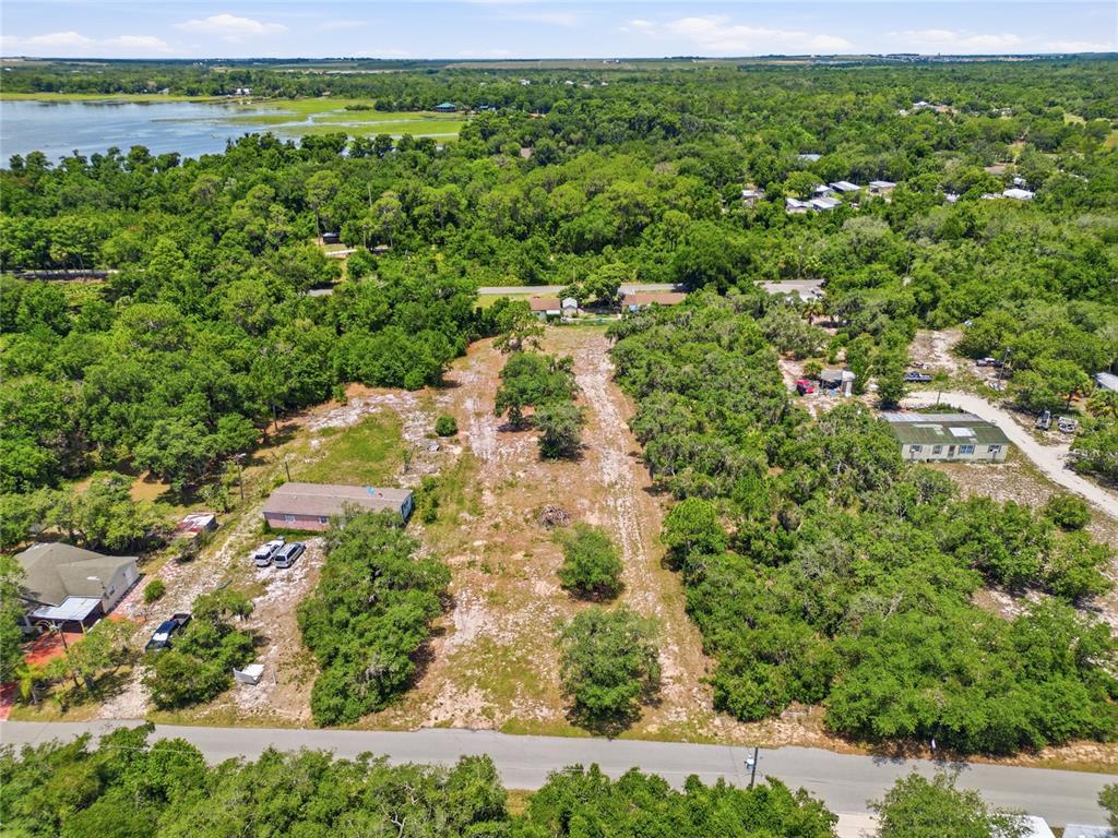 An aerial view shows a vacant, wooded lot situated between two houses near a lake — HARTMAN RD, LAKE WALES, FL