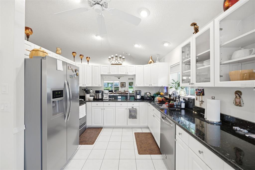 A kitchen with white cabinets, black countertops, stainless steel appliances, and white tile flooring — 14458 TAMARIND LOOP, SPRING HILL, FL