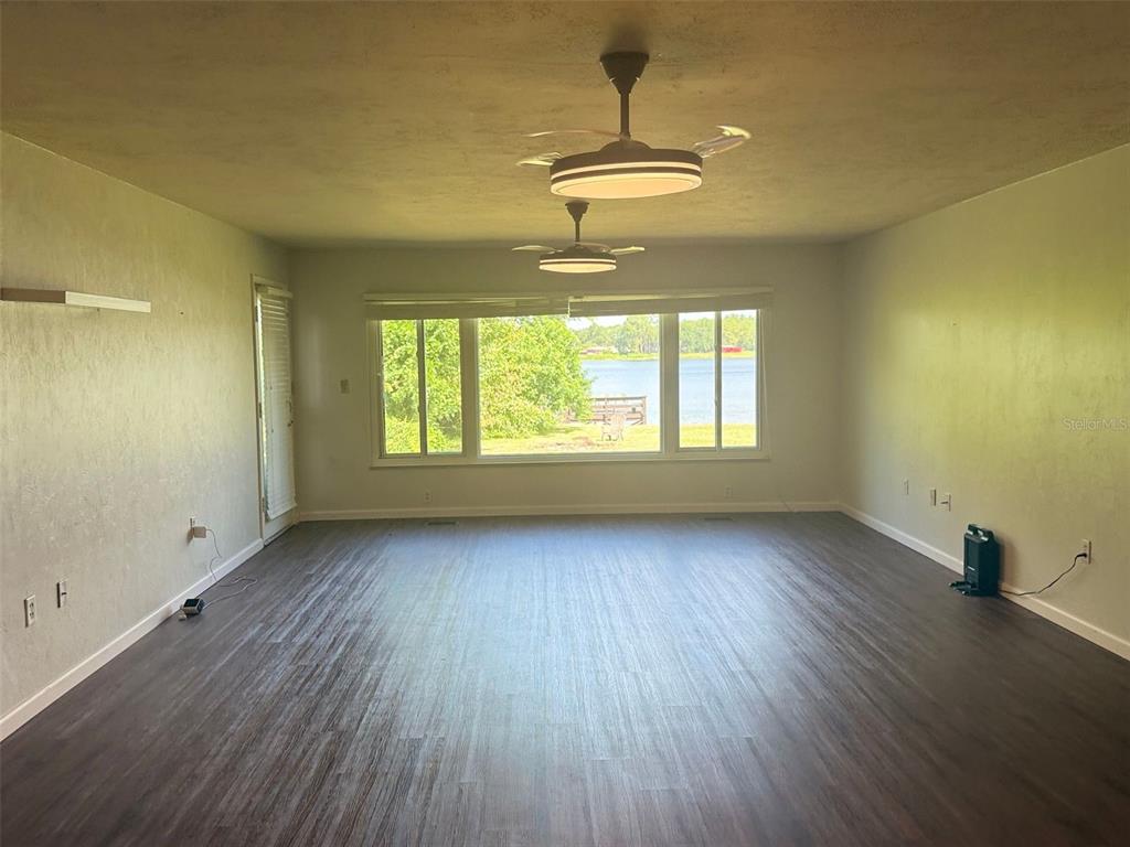 A living room with dark wood-look flooring, two ceiling fans, and a large windowed view — 1932 CRESCENT BOULEVARD, ORLANDO, FL