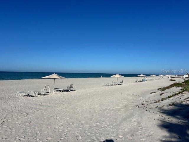 A sandy beach features several umbrellas and lounge chairs under a clear blue sky — 1095 GULF OF MEXICO DRIVE UNIT 104, LONGBOAT KEY, FL