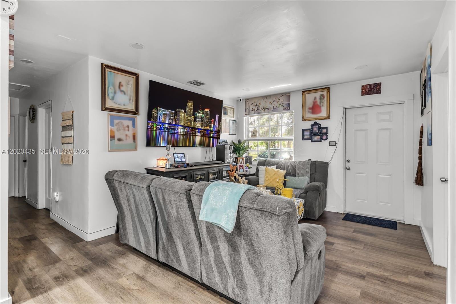 A living room features gray sofas, a wall-mounted television, and wood-look flooring — 13075 NW 16th Ave, North Miami FL 33167, NORTH MIAMI, FL