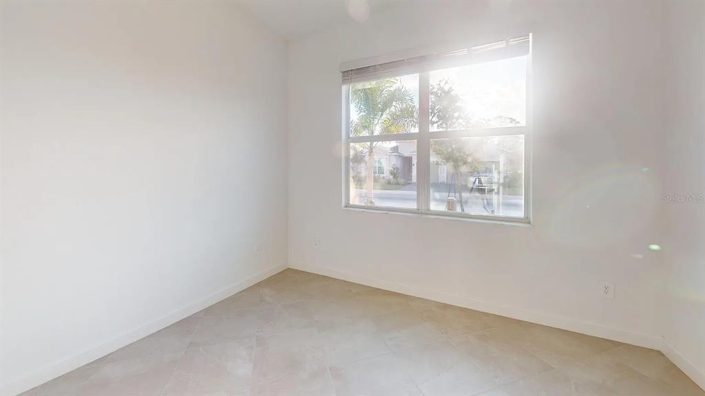 An empty room features white walls, light-colored tile flooring, and a large window — 8535 SAINT KITTS CIRCLE, ENGLEWOOD, FL