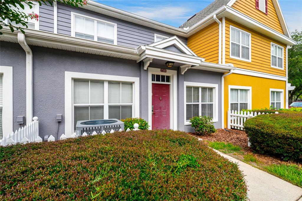 A two-story townhouse exterior features gray and yellow siding, a red door, and landscaping — 4562 JONAFREE LANE UNIT 106, KISSIMMEE, FL