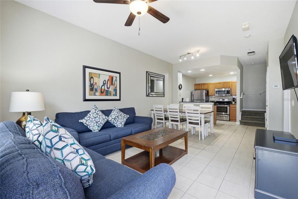 A living room with blue sofas and a dining area adjacent to a kitchen — 4562 JONAFREE LANE UNIT 106, KISSIMMEE, FL