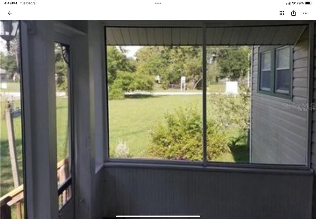 A view from inside a screened-in porch looking out onto a grassy yard — 5612 WOODWARD AVENUE, ZELLWOOD, FL