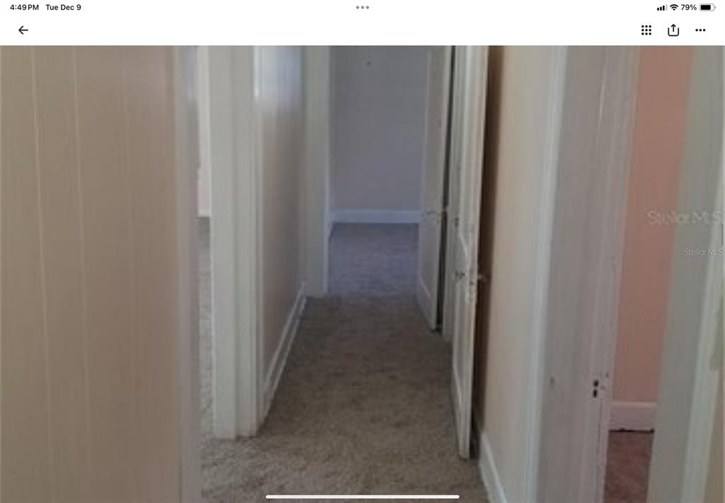 A hallway with beige carpet leads to an open doorway showing another carpeted room — 5612 WOODWARD AVENUE, ZELLWOOD, FL