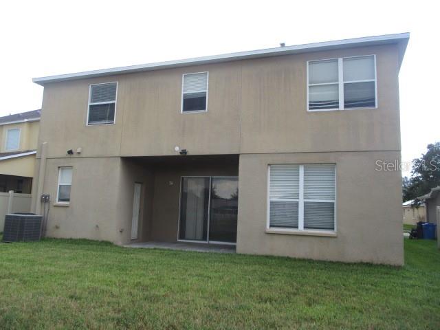 The rear exterior of a two-story beige stucco house features a covered patio and lawn — 20123 STILL WIND DRIVE, TAMPA, FL