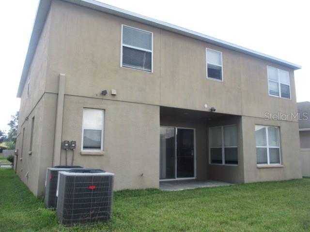 The back exterior of a two-story tan stucco house features a covered patio and AC units — 20123 STILL WIND DRIVE, TAMPA, FL