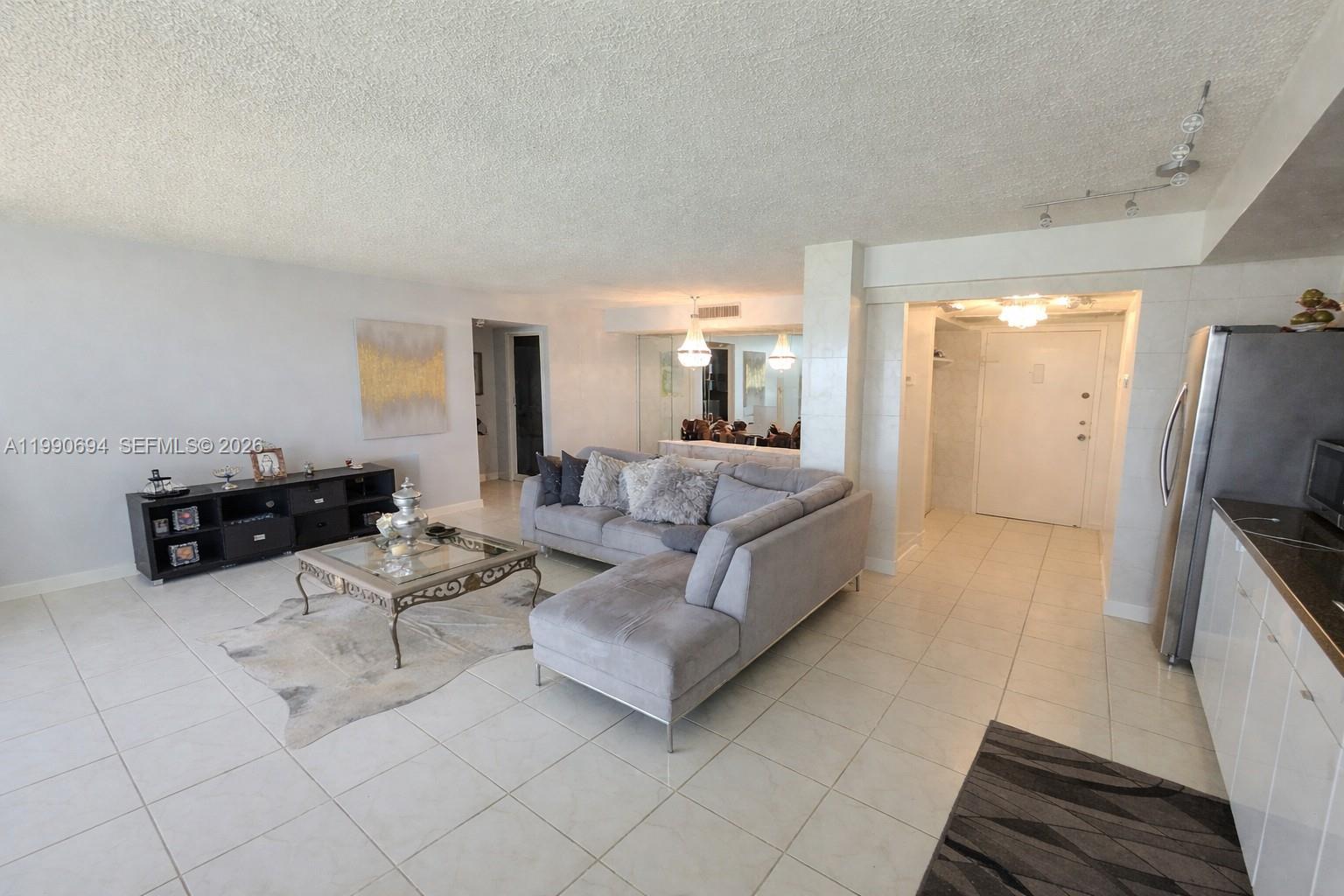 A living room features light tile flooring, a gray sectional sofa, and a glass coffee table — 701 Three Islands Blvd # 510, Hallandale Beach FL 33009, HALLANDALE BEACH, FL