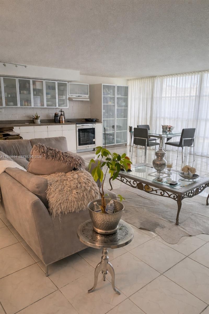 A living room and kitchen area with tile floors, a glass coffee table, and dining set — 701 Three Islands Blvd # 510, Hallandale Beach FL 33009, HALLANDALE BEACH, FL