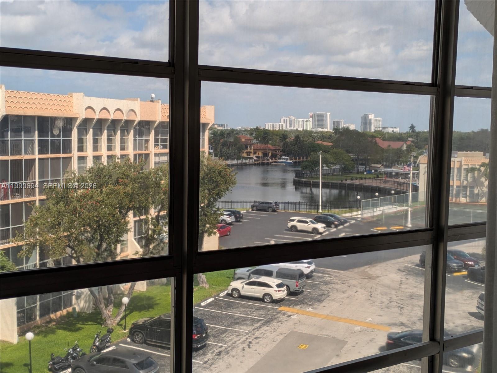 A view from a window overlooks a parking lot, a waterway, and distant city buildings — 701 Three Islands Blvd # 510, Hallandale Beach FL 33009, HALLANDALE BEACH, FL