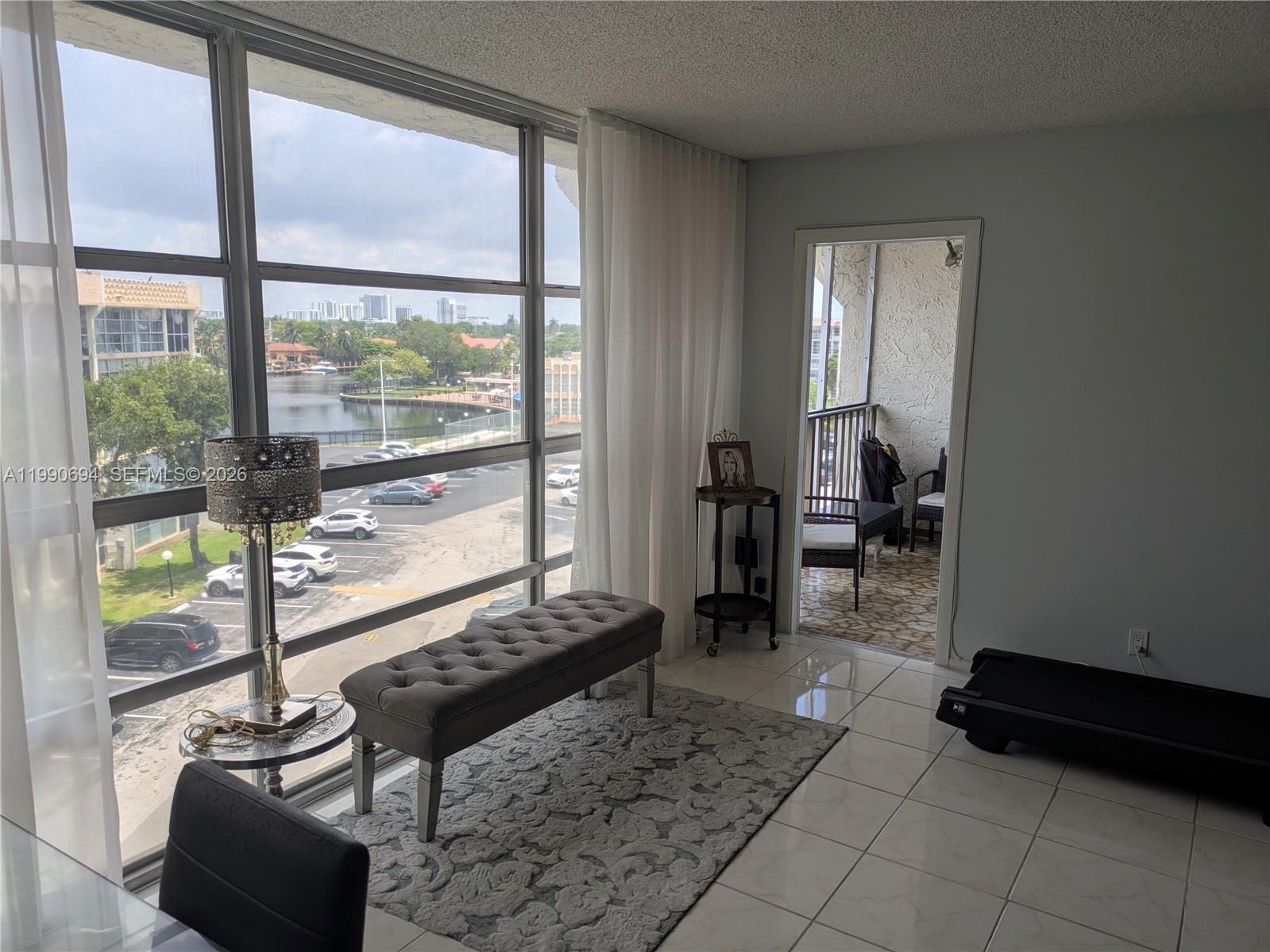 A living area features floor-to-ceiling windows, a tufted bench, tile flooring, and a balcony — 701 Three Islands Blvd # 510, Hallandale Beach FL 33009, HALLANDALE BEACH, FL