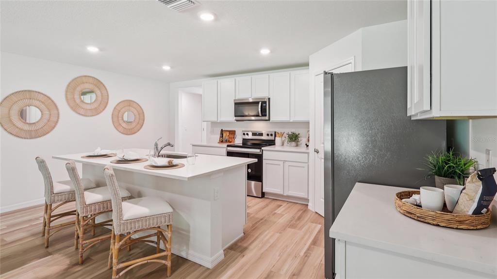 A modern kitchen features white cabinetry, a central island with bar seating, and wood flooring — 8395 CLEARWAY DRIVE, WILDWOOD, FL