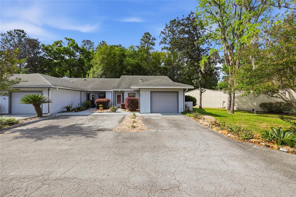 A single-story house with two garage doors and a paved driveway sits among trees — 6617 NW 114TH LANE UNIT 6617, ALACHUA, FL