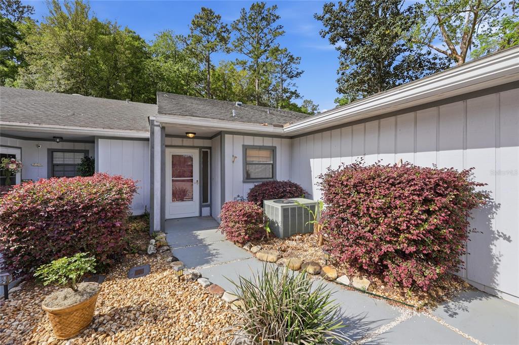 A white house exterior features a front entrance, a concrete walkway, and landscaped bushes — 6617 NW 114TH LANE UNIT 6617, ALACHUA, FL