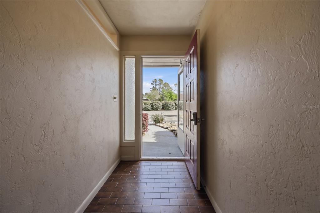 An entryway with brown tile flooring and a red front door opening to the outdoors — 6617 NW 114TH LANE UNIT 6617, ALACHUA, FL