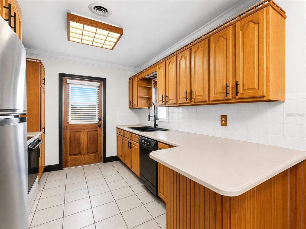 A kitchen features oak cabinets, light countertops, a black dishwasher, and a wood-paneled exterior door — 5320 41ST AVENUE W, BRADENTON, FL