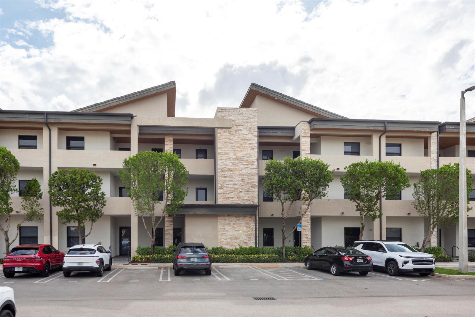 A three-story apartment building exterior features tan stucco, stone accents, and a parking lot — 7925 NW 104th Avenue # 24, Doral FL 33178, DORAL, FL