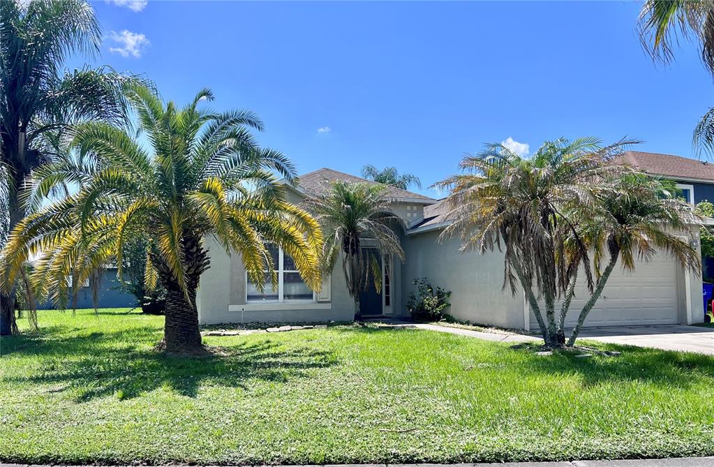 A single-story house with a light-colored exterior, a two-car garage, and several palm trees — 2950 ELBIB DRIVE, ST CLOUD, FL
