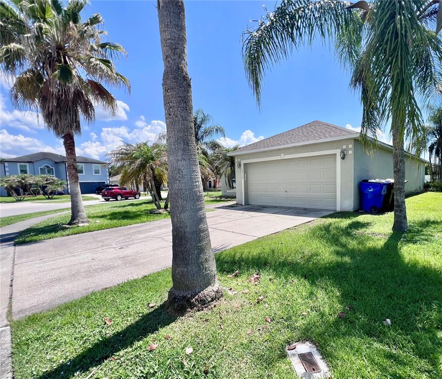 A view of a house exterior featuring a two-car garage, concrete driveway, and palm trees — 2950 ELBIB DRIVE, ST CLOUD, FL
