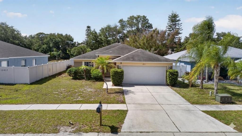 A single-story house with a two-car garage, a concrete driveway, and a white vinyl fence — 12015 CEDARFIELD DRIVE, RIVERVIEW, FL