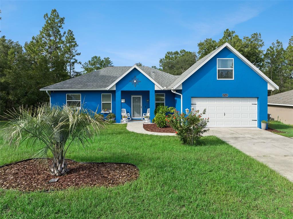 A bright blue single-story house features a white garage door and a front lawn — 8742 SW 135TH STREET ROAD, OCALA, FL