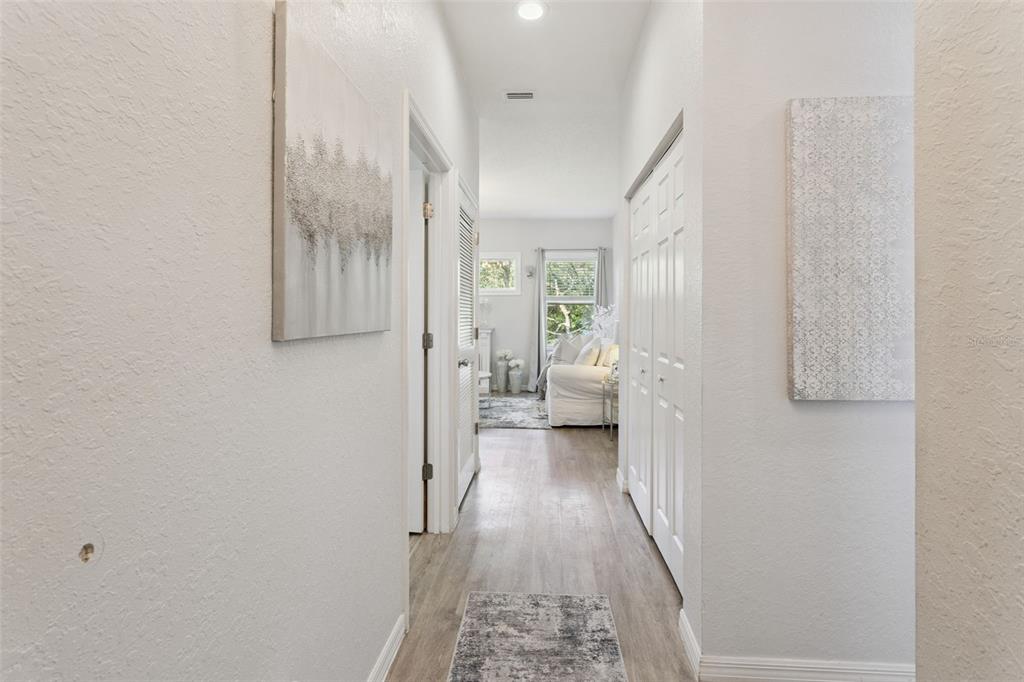 A hallway with light wood-look flooring leads to a bright room with a white sofa — 8742 SW 135TH STREET ROAD, OCALA, FL