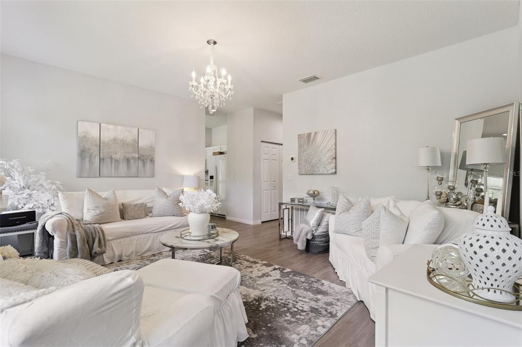 A bright living room features white sofas, a crystal chandelier, and a patterned area rug — 8742 SW 135TH STREET ROAD, OCALA, FL