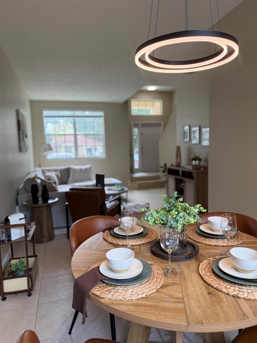 A dining area with a round wooden table and modern pendant light overlooks a living room — 5203 Eagle Cay Place, Coconut Creek FL 33073, COCONUT CREEK, FL