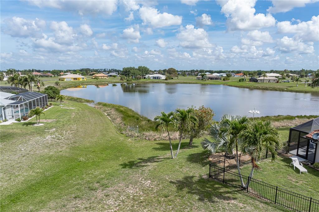 An elevated view of a backyard lawn, palm trees, a lake, and surrounding residential houses — 17528 VELLUM CIRCLE, PUNTA GORDA, FL