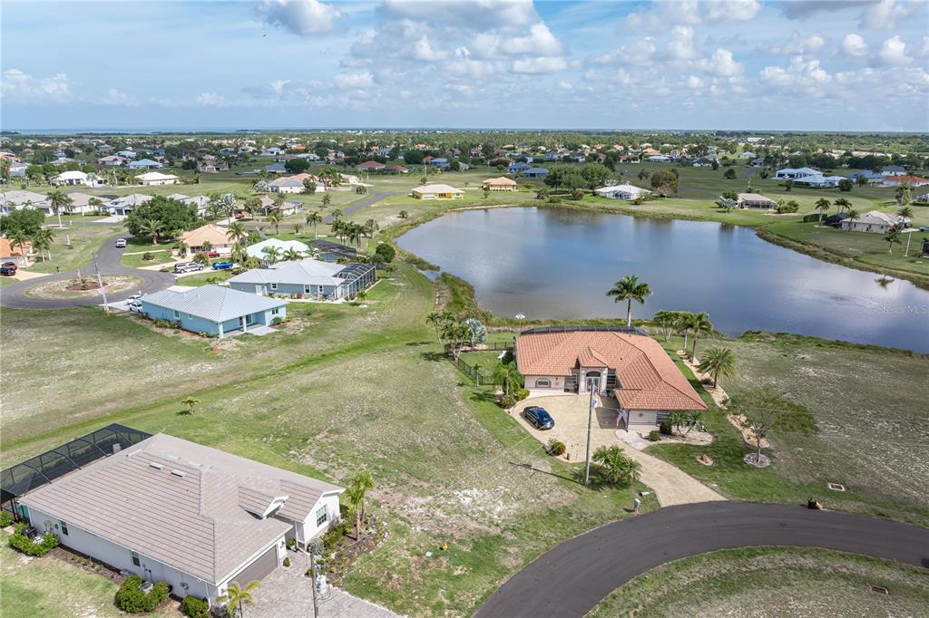 An aerial view shows several suburban houses, a large pond, and surrounding grassy lots — 17528 VELLUM CIRCLE, PUNTA GORDA, FL