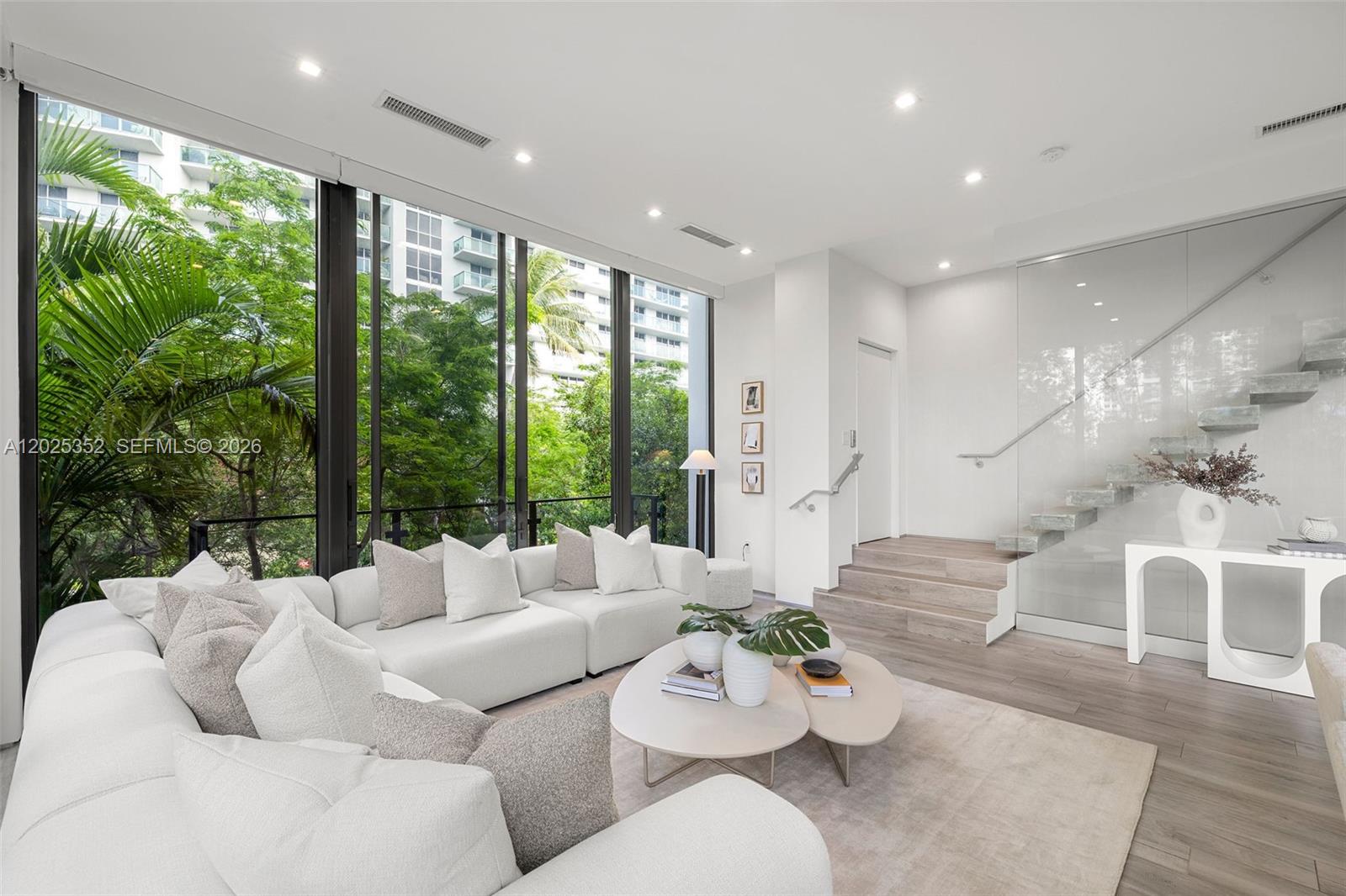 A modern living room features a large white sectional sofa, floor-to-ceiling windows, and floating stairs — 1525 Bay Rd, Miami Beach FL 33139, MIAMI BEACH, FL
