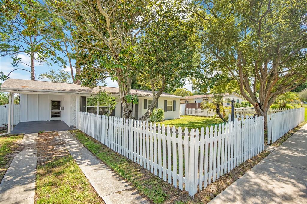 A single-story house with a white picket fence, a carport, and mature trees in front — 682 MERRIMAC STREET, DELTONA, FL