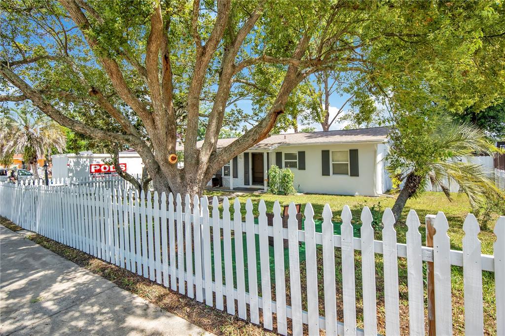 A white single-story house sits behind a white picket fence under a large tree — 682 MERRIMAC STREET, DELTONA, FL