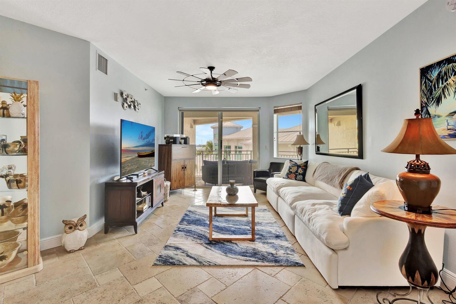 A living room features tile flooring, a white sofa, a television, and a balcony view — 975 NW Flagler Avenue # 407, Stuart FL 34994, STUART, FL